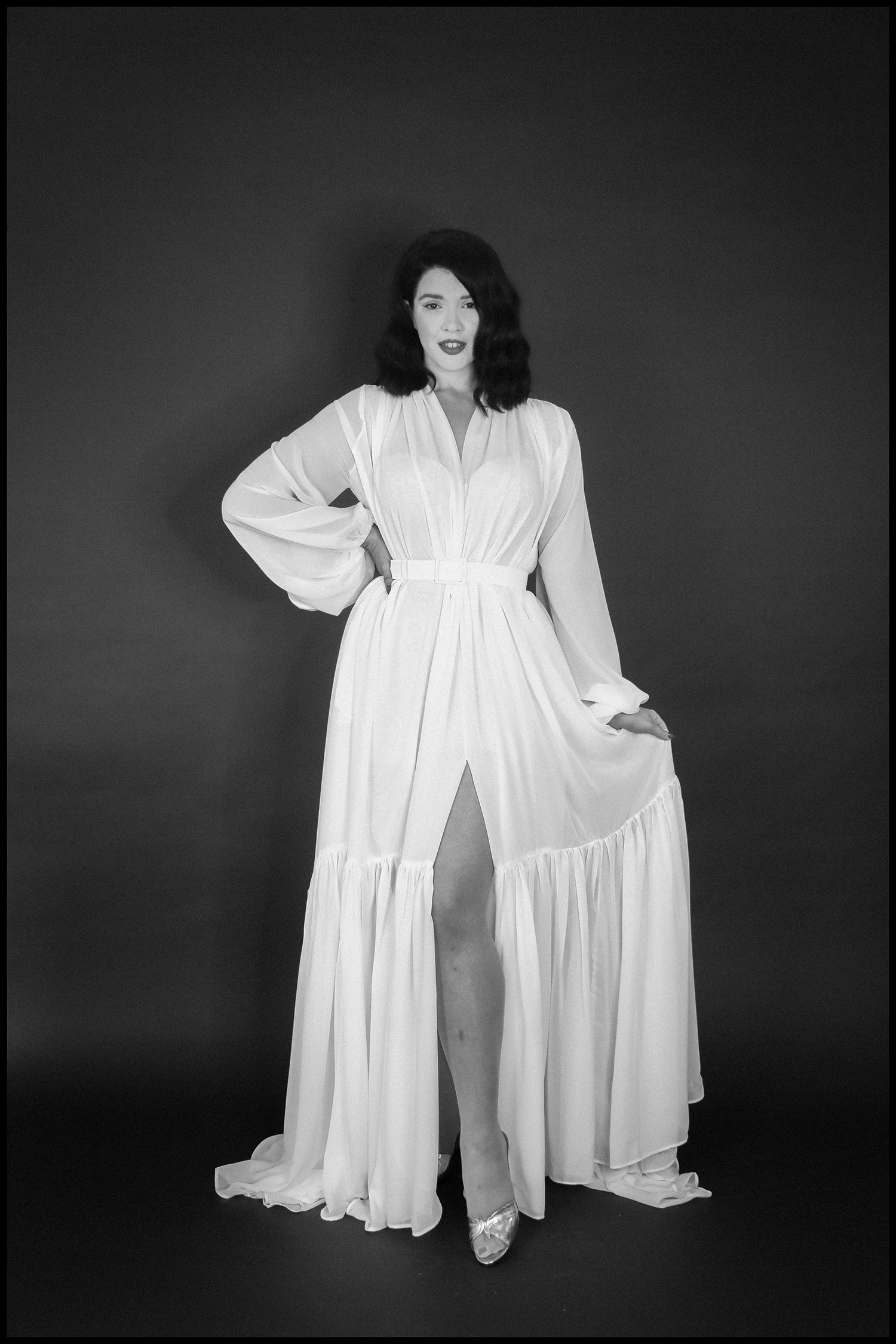 Black and white portrait of a person wearing a long, flowing white dress against a dark background.