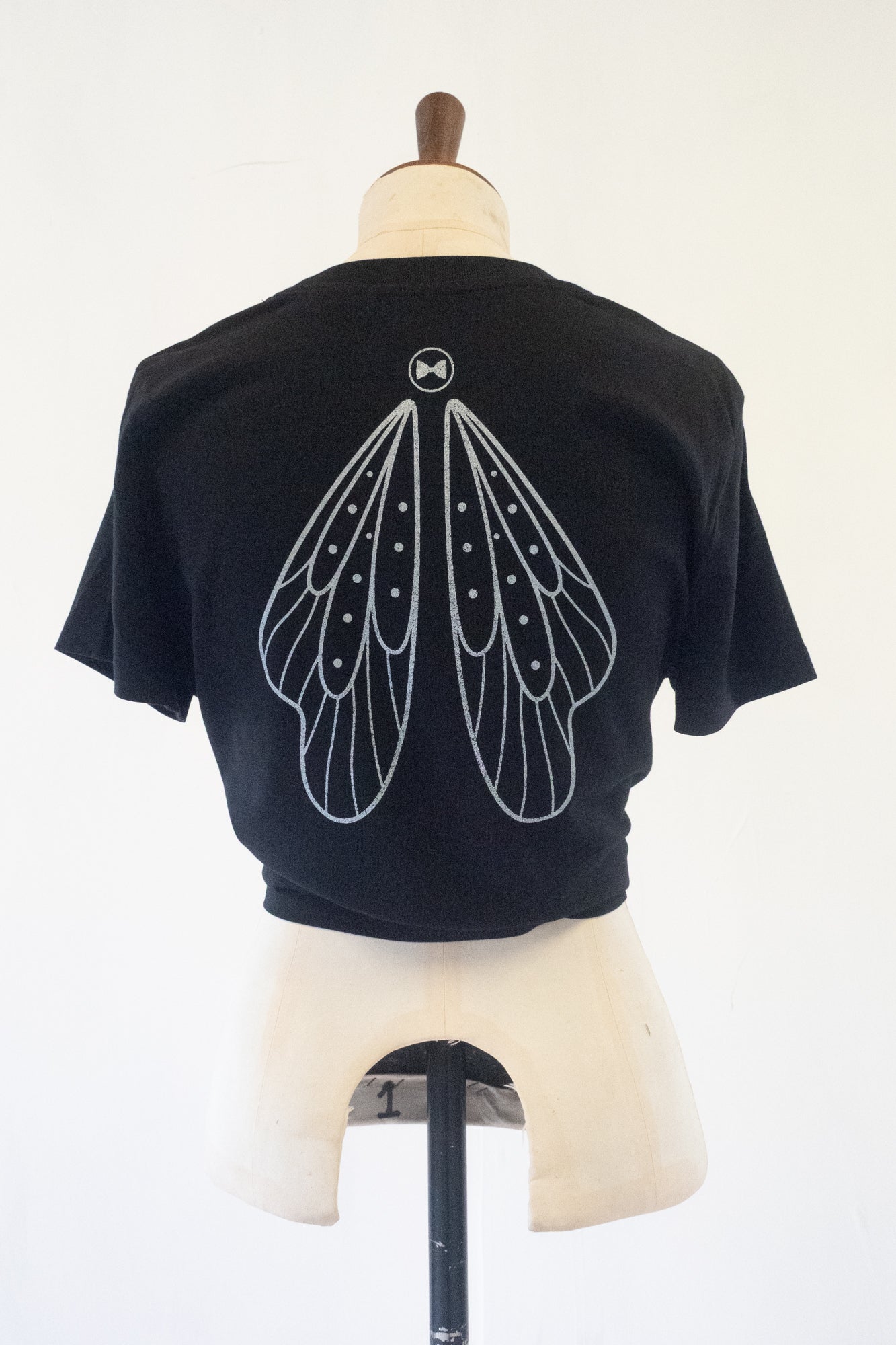 Black t-shirt with silver metallic fairy wing design on a mannequin against a white background