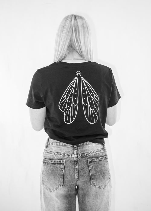 Person wearing a black t-shirt with fairy wings design on the back against a white background by Alexandra King