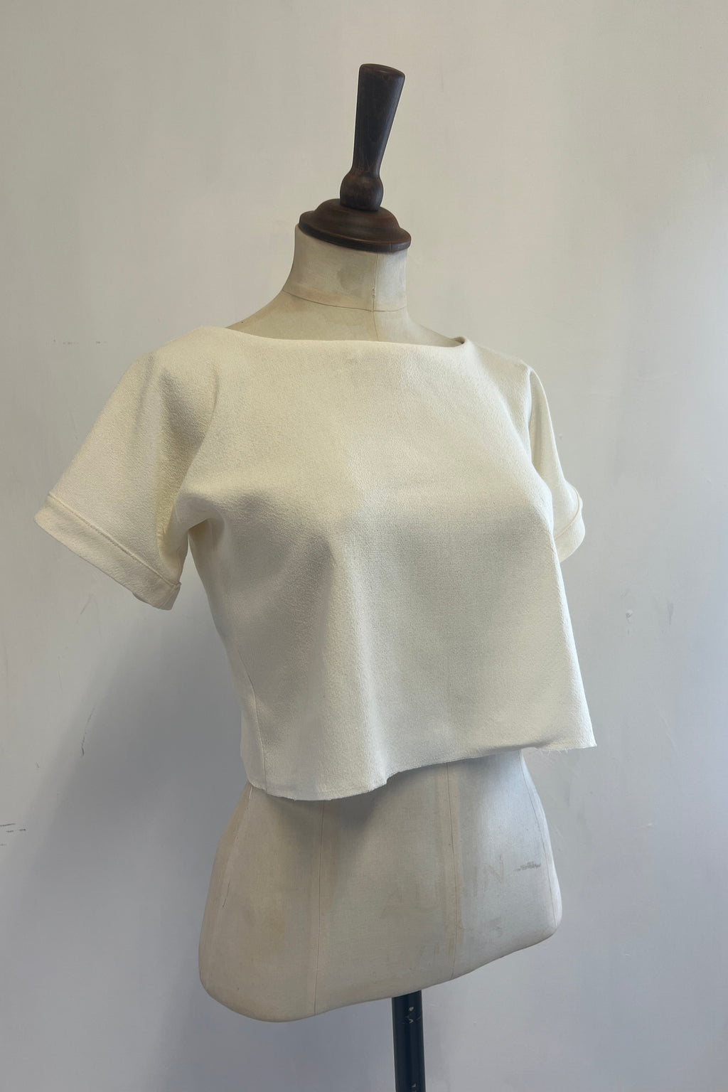 A beige t-shirt on a mannequin, displaying a cropped cut with cuffed sleeves and a keyhole back.