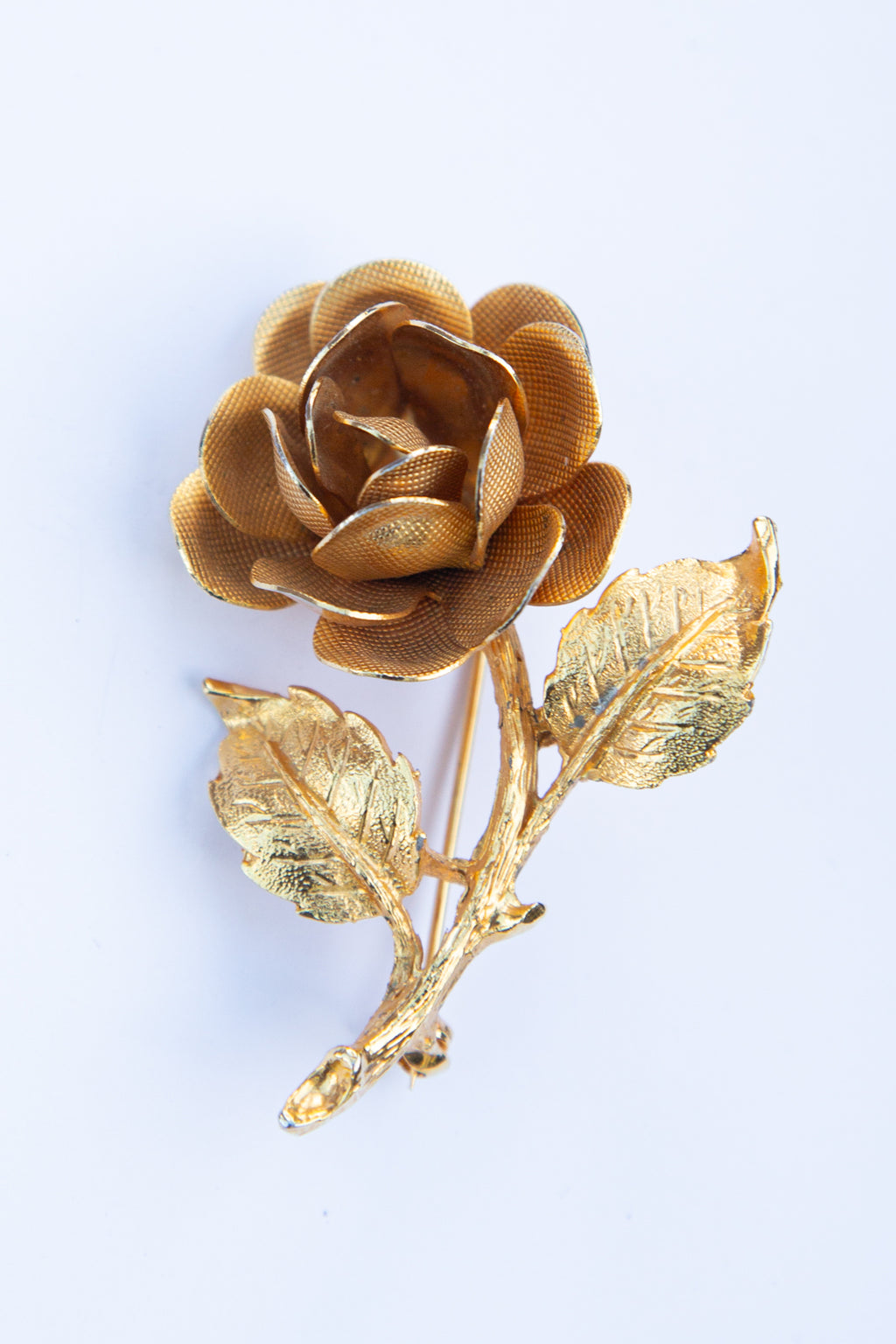 Gold rose brooch with leaves on a light blue background