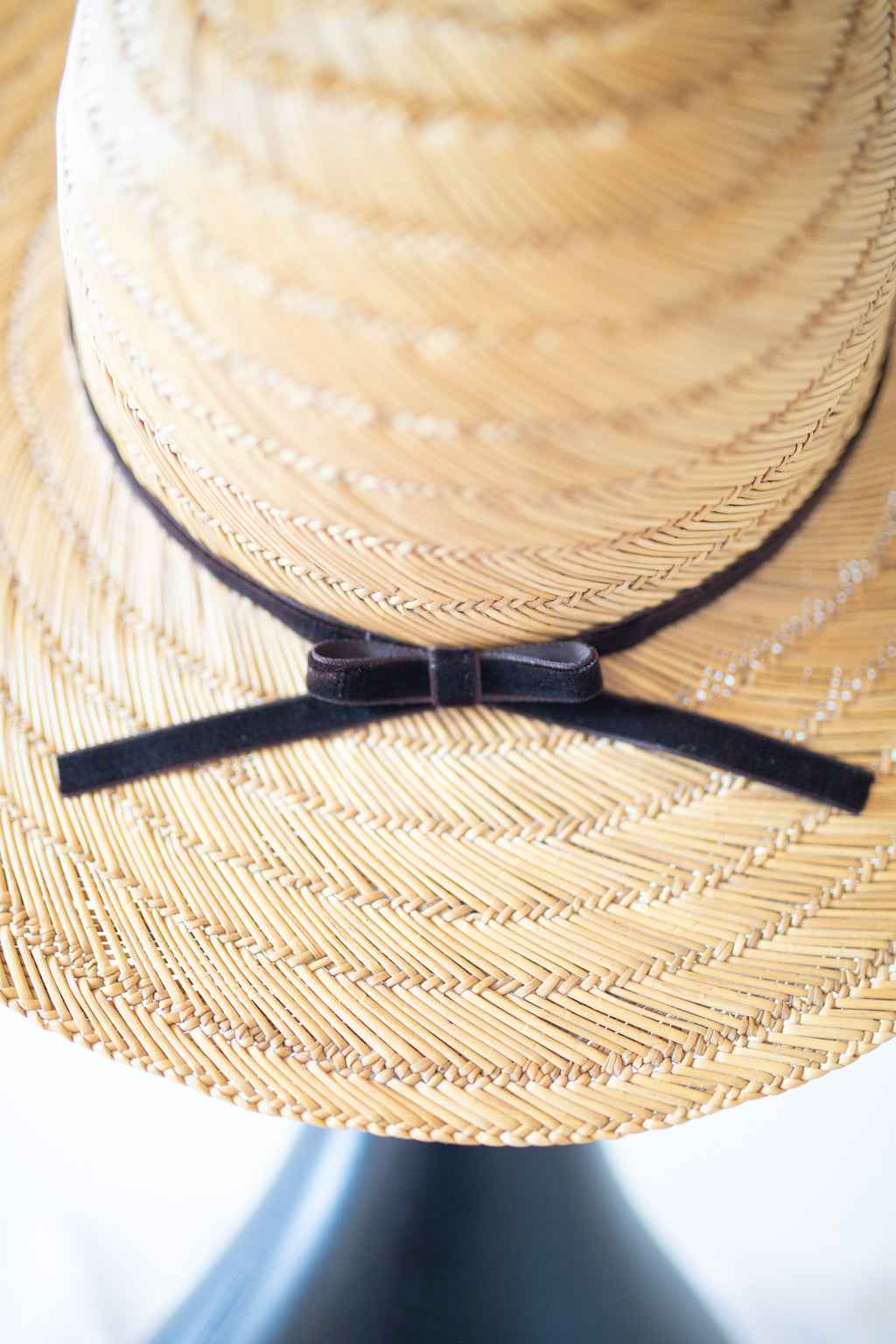 Close-up of a woven straw sun hat with a black ribbon band and bow on a dark display stand.