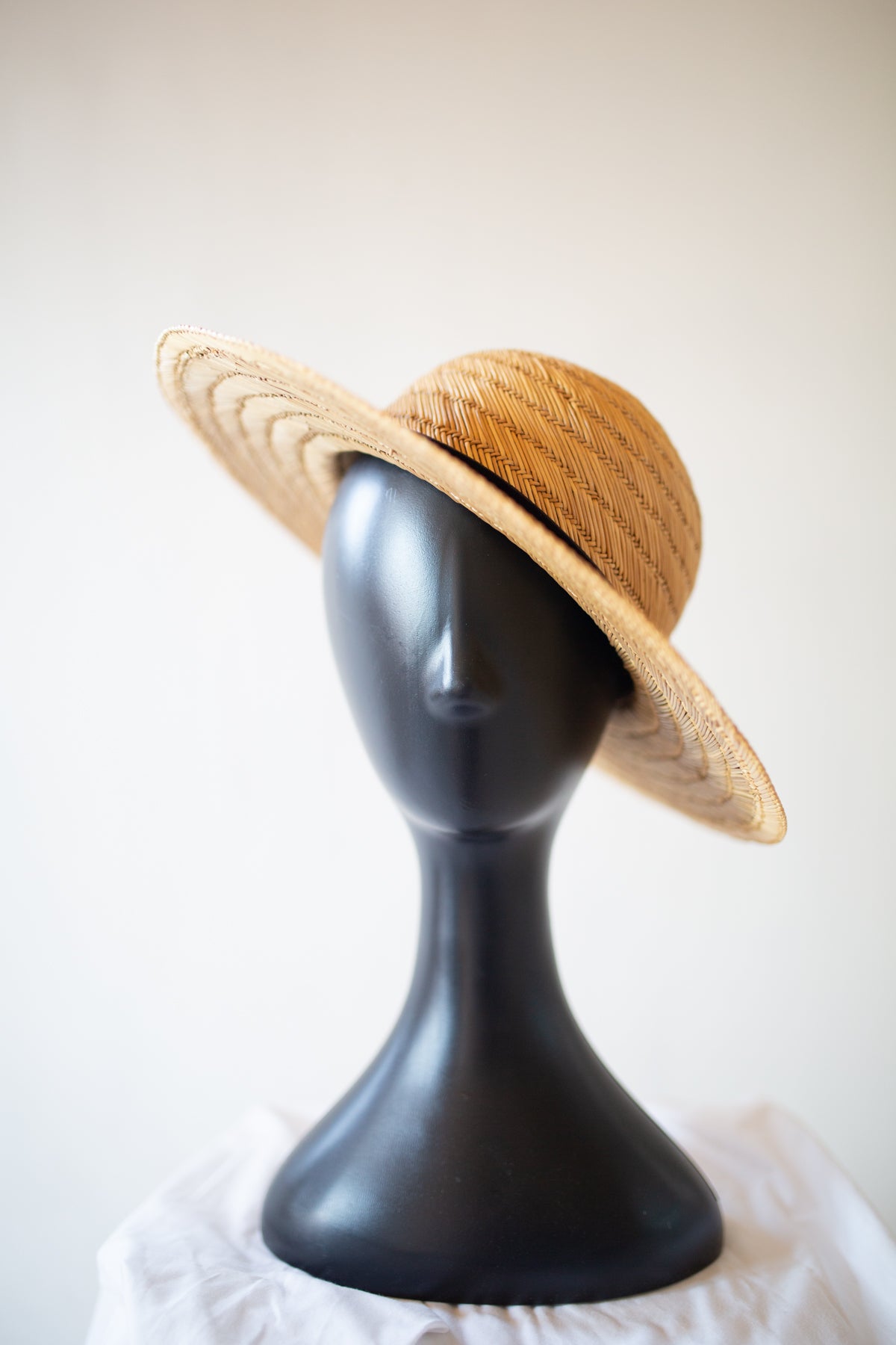 A woven straw sun hat in a natural tan color, displayed on a matte black mannequin head against a light off-white background.