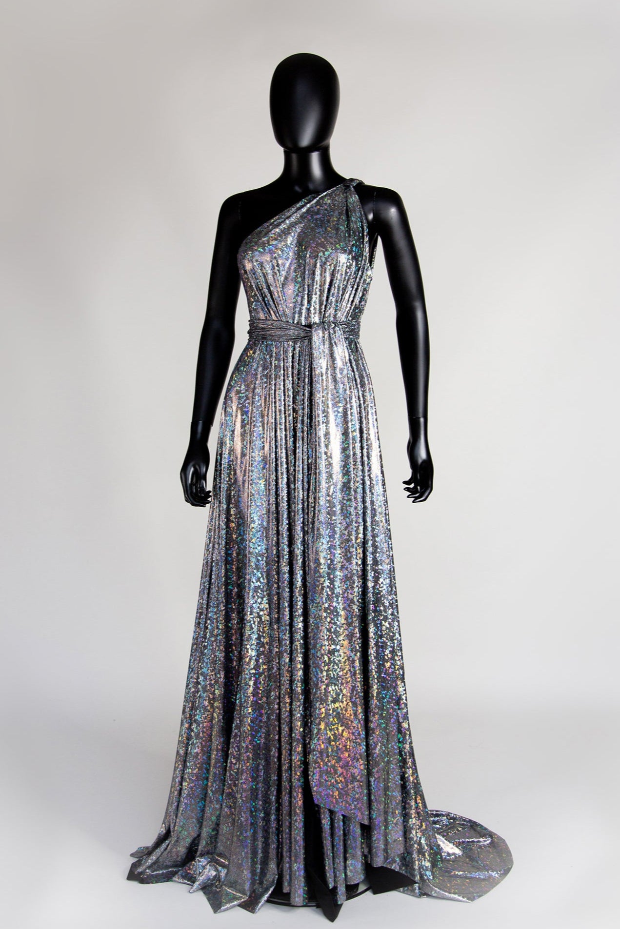 A silver holographic gown with asymmetric draping and a one-shoulder neckline, displayed on a mannequin.