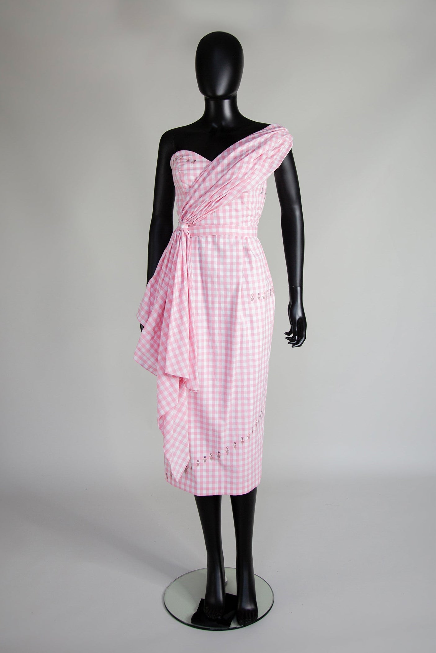 A mannequin displaying a pink gingham cotton midi dress with a sweetheart bodice and a pencil skirt.