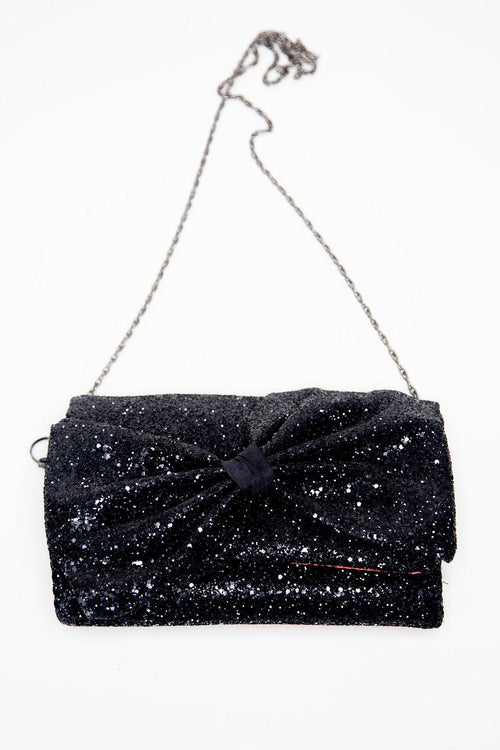 A black glittery clutch bag with a large asymmetric bow over the flap and a chain strap.