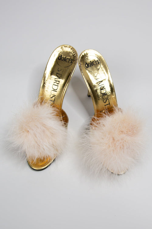 A pair of shoe clips with fluffy marabou style feathers in ivory and champagne colors, attached to metal shoe clips and positioned on a white background.