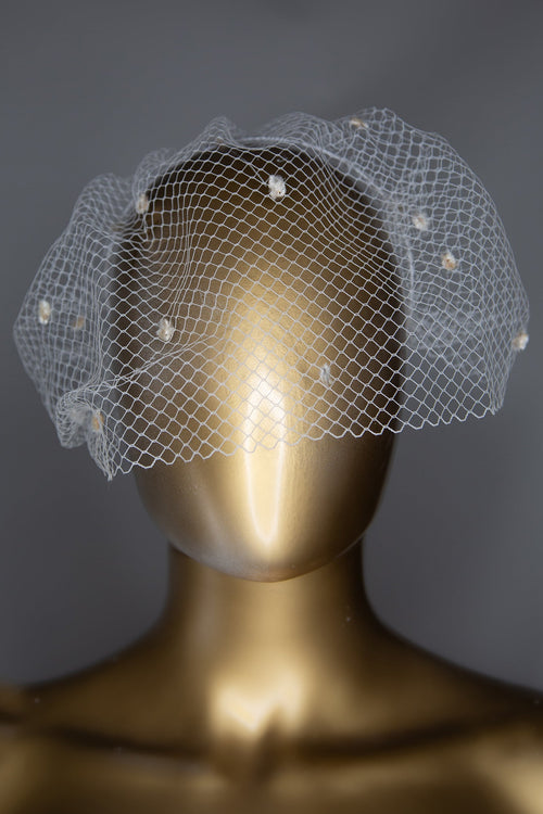 A mannequin head featuring an ivory dot birdcage veil headpiece with velvet dot detailing, displayed on a stand.