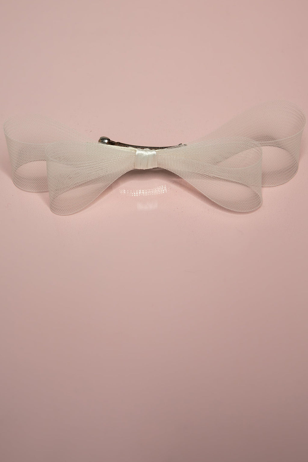 A double hair bow with a cream-colored crinoline and satin center, mounted on a barrette clip, displayed against a pink background.