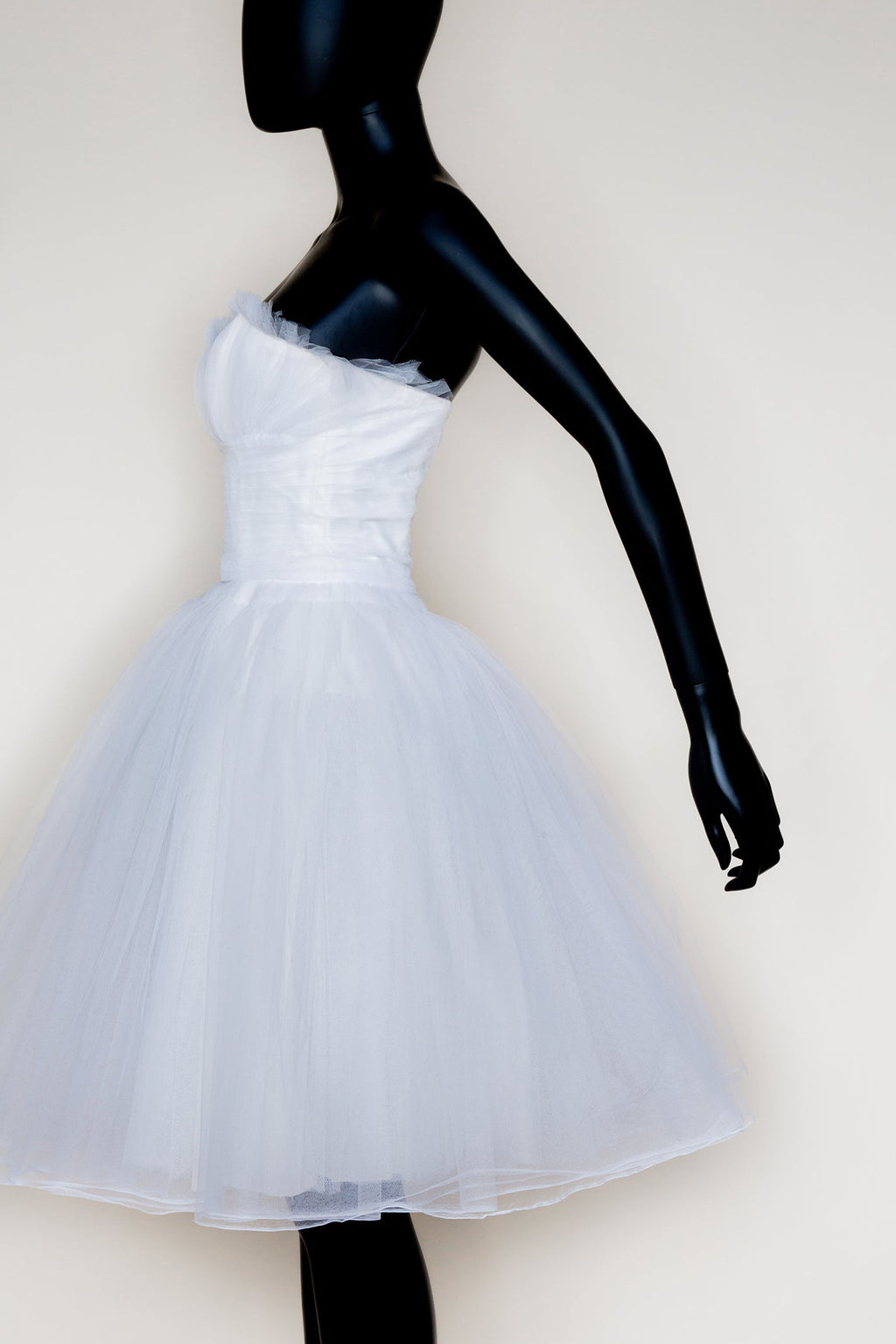 A white tulle prom dress with a strapless design, featuring a gathered ruffle bust, fine pleated long line cut skirt, and a concealed zip back.