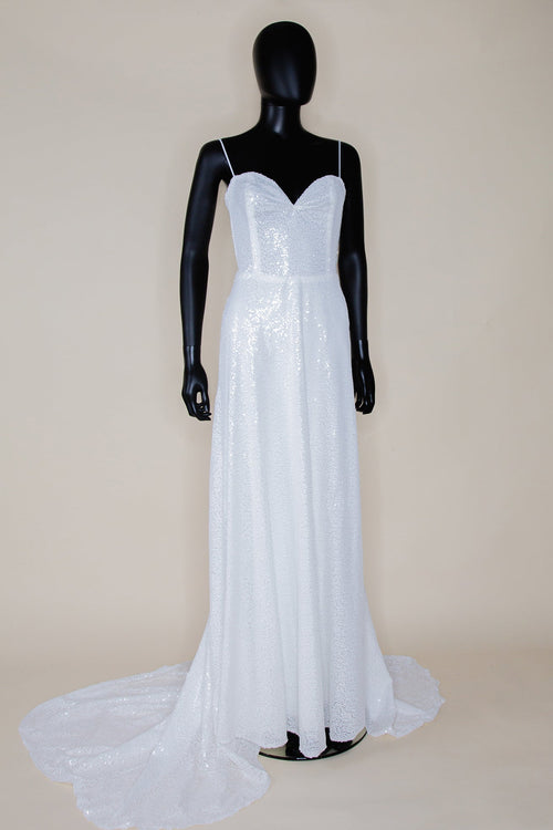 White sequin gown with a sweetheart boned bodice, fine velvet straps, and a long chapel train skirt. Displayed on a mannequin against a black background.